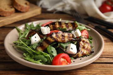 Delicious salad with roasted eggplant, feta cheese and arugula served on wooden table, closeup