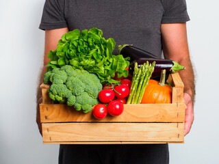 Wooden box with vegetables in a man's hands.