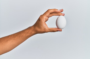 Fototapeta na wymiar Young hispanic hand holding raw egg over isolated white background.