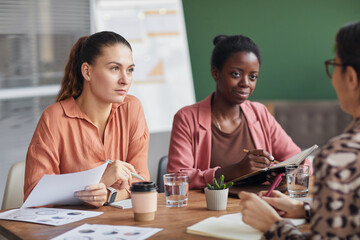 Portrait of multi-ethnic female business team discussing project while sitting at meeting table in conference room, copy space