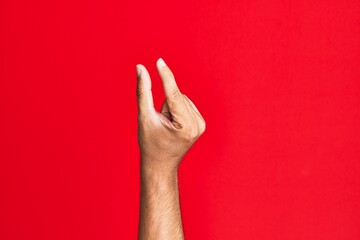 Arm of caucasian white young man over red isolated background picking and taking invisible thing, holding object with fingers showing space