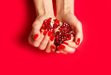 Red fresh pomegranate in woman's hand, fingernails with red nail polish on red background. Close up.