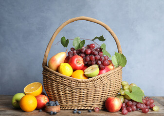 Wicker basket with different fruits and berries on wooden table near blue wall