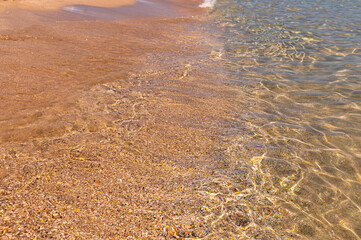 Calm morning sea beach with small waves with foam and clear water
