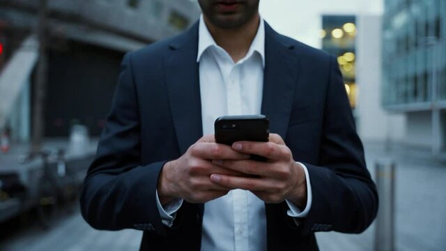 Close up businessman typing on cellular device walking home after work 