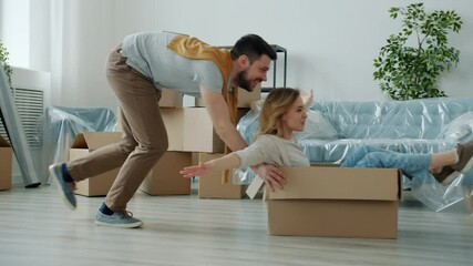 Slow motion of girl and guy having fun riding carton boxes relocating to new apartment enjoying leisure time together. People and youth lifestyle concept.