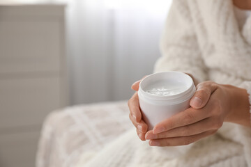 Fototapeta na wymiar Woman with jar of moisturizing cream indoors, closeup