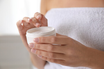 Woman with jar of moisturizing cream on blurred background, closeup
