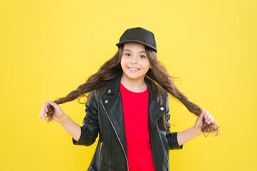 Happy small girl child with beauty look in casual fashion style hold long brunette hair yellow background, haircare