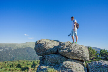 Naklejka na ściany i meble Man in sportswear on a big rock seeing the green valley on a sunny day