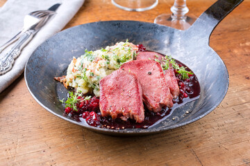 Traditionelle gebratene Rinderzunge mit Kartoffel Püree und Preiselbeeren Relish serviert als close-up in einer rustikalen schmiedeeisernen Pfanne auf einem Holzboard
