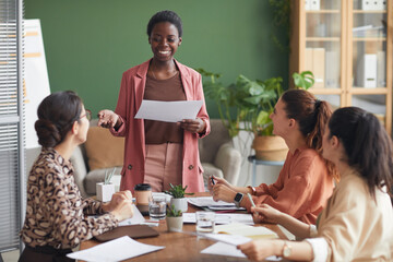 Fototapeta premium Portrait of successful African-American businesswoman holding documents while heading meeting with female team in office, copy space