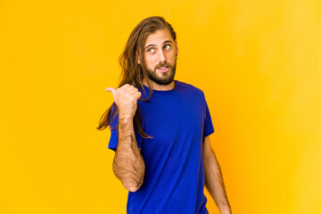 Young man with long hair look points with thumb finger away, laughing and carefree.