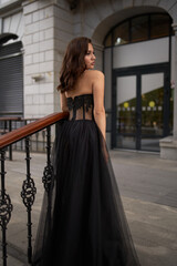 Full-length portrait of an elegant brunette woman with long hair in a black long evening dress.