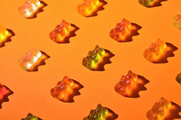 Assortment of colored gummy bears on an orange background and with the reflection to their side of the hard light passing through them