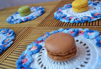 Several macarons on  white crochet doily with a blue and pink flower trim on a wooden table