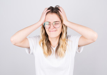 Woman in eyeglasses with a headache holds her temples with her hands. Health, migraine and headache concept.