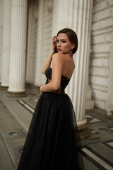 Obraz premium Full-length portrait of an elegant brunette woman with long hair in a black long evening dress.