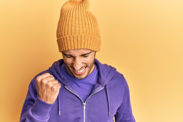 Young handsome man wearing wool winter hat celebrating surprised and amazed for success with arms...