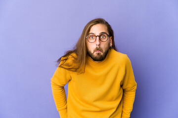 Young man with long hair look shrugs shoulders and open eyes confused.