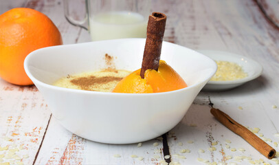 Close up  the homemade rice pudding, with a touch of citrus and cinnamon, in a white porcelain bowl on white rustic woods.