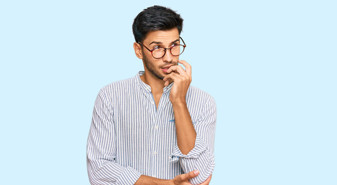 Young handsome man wearing casual clothes and glasses looking stressed and nervous with hands on mouth biting nails. anxiety problem.
