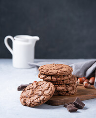 a stack of chocolate chip cookies with chocolate chips and  nuts with jug on a light table