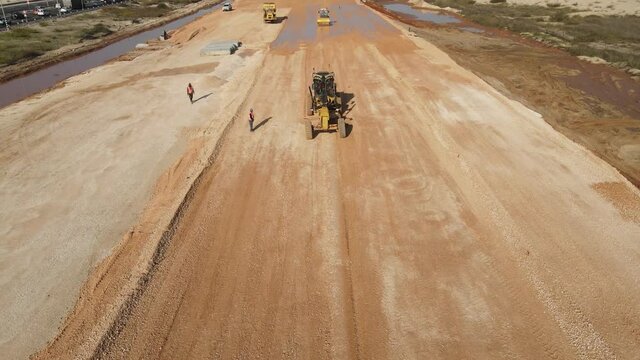 Aerial view of heavy machinery, motor grader spreader gravel in preparation for road construction. heavy equipment top down footage
