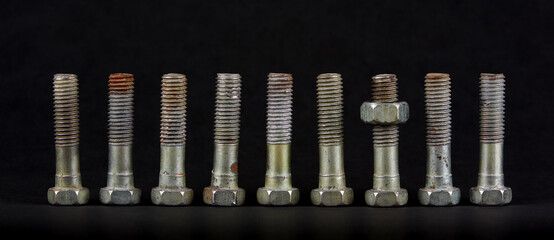 Nine bolts with nuts in a row on black background. One object differs from the rest in position. The part has a nut.