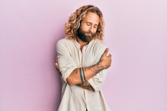 Handsome man with beard and long hair wearing casual clothes hugging oneself happy and positive, smiling confident. self love and self care