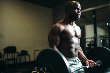 Fototapeta na wymiar Strong man bodybuilder african american with a naked torso holds a barbell in his hands, lifts a heavy weight, prepares for a competition in the gym