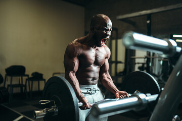 Fototapeta na wymiar Emotional muscular african american man straining muscles, screaming and lifting a heavy barbell
