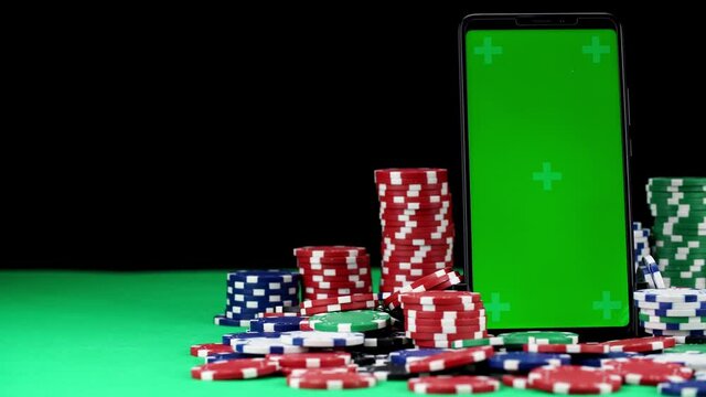 Mobile with green screen in a vertical orientation stands among stacks of poker chips in close-up. Playing at hazard games in online casino. Winning and losing money. Concept of gambling in real time.