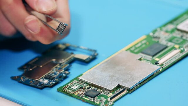 Worker removing broken item from circuit board with tweezers. Hands closeup.