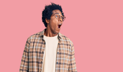 Handsome african american man with afro hair wearing casual clothes and glasses angry and mad screaming frustrated and furious, shouting with anger. rage and aggressive concept.