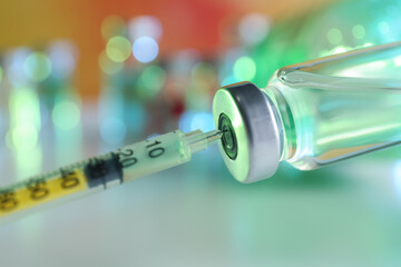 Filling syringe with medication from vial against blurred background, closeup. Vaccination and immunization