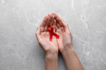Woman holding red awareness ribbon at light grey marble table, top view. World AIDS disease day