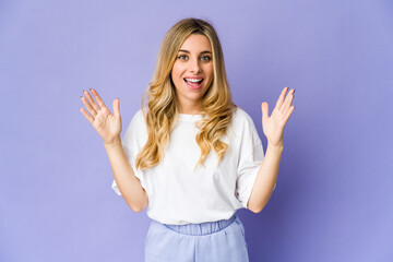 Young caucasian blonde woman receiving a pleasant surprise, excited and raising hands.