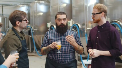 Young people tasting beer and listening to brewer during tour in factory