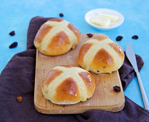 Traditional Easter cross buns made from yeast dough on a wooden board against a blue concrete background. Easter holiday, concept. Easter recipes.