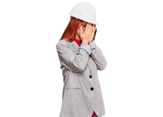 Young redhead woman wearing architect hardhat with sad expression covering face with hands while crying. depression concept.