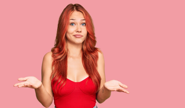 Young redhead woman wearing casual clothes clueless and confused expression with arms and hands raised. doubt concept.