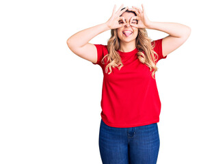 Young caucasian woman wearing casual clothes doing ok gesture like binoculars sticking tongue out, eyes looking through fingers. crazy expression.