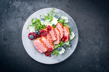 Modern style gourmet duck breast filet with rocket salad and cranberry relish served as top view on a design plate with copy space