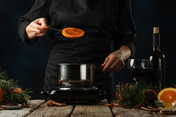 The chef took the orange out of the pan for preparing mulled wine on rustic wooden table with...