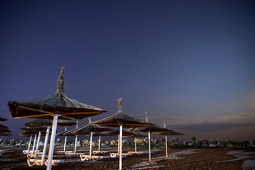 Umbrellas on the beach at night with stars on the sky	
