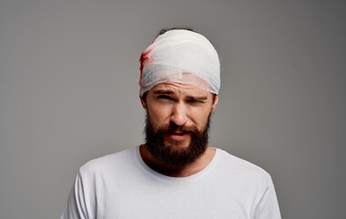 a man with a bandaged head blood on his arm operation gray background white t-shirt
