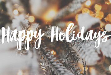 Happy holidays Greeting card. Happy holidays text handwritten on stylish snowy christmas tree branches with golden lights. Modern Seasons greetings © sonyachny
