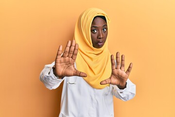Beautiful african young woman wearing doctor uniform and hijab moving away hands palms showing refusal and denial with afraid and disgusting expression. stop and forbidden.