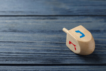 Hanukkah traditional dreidel with letters Nun and Gimel on blue wooden table. Space for text